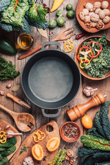 Various organic vegetables ingredients and empty iron cooking pot, wooden bowls, spoons on wooden...