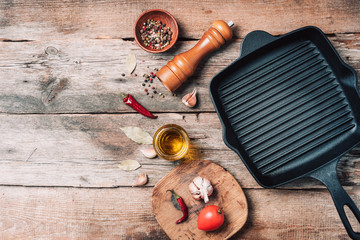 Cast iron pan, spices, pepper shaker, meat fork, oil, spices on wooden background. Top view. Copy space. Healthy, clean food and eating concept. Zero waste. Cooking ingredients frame