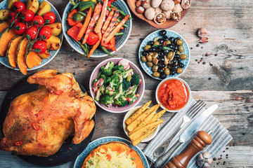 Thanksgiving dinner cooking preparation. Traditional dishes: chicken, pumpkin, corn, vegetables salads over wooden background. Top view, copy space. Autumn harvest, organic vegetables. Family dinner
