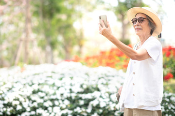 Asian retired woman using smart phone for taking picture during her vacation. Elderly people and communication technology device concept