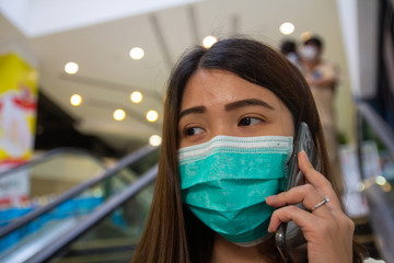 Fototapeta na wymiar Asian woman wearing protective face masks against air pollution (PM2.5), prevent Coronavirus and talking on phone in public mall. Sick female with flu wearing mask.