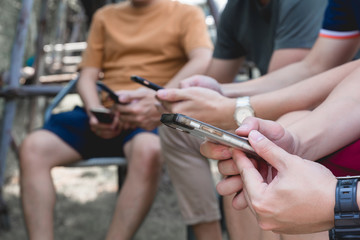 Closeup group friends hands holding modern smartphone chatting in the park.