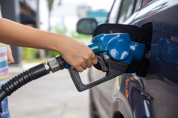 Blue car at gas station filled with fuel. Closeup woman hand pumping gasoline fuel in car at gas...