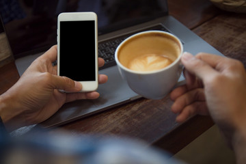 Man hands holding mobile phone with blank black screen and drinking coffee cup in cafe.