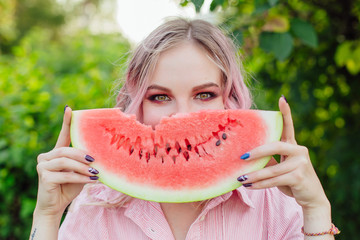 Beautiful young woman with pink hair holding juicy watermelon close to the face