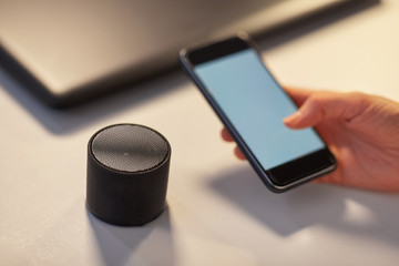 business, technology and internet of things concept - hand with smartphone and smart speaker at...