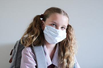Schoolgirl wearing surgical mask and backpack in school uniform during Covid-19 / coronavirus pandemic