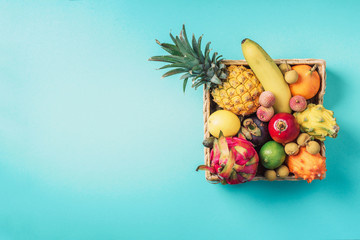 Tropical fruits on blue background. Rattan box full of exotic thailand fruits - pineapple, pitahaya, kiwano, african horned melon, tamarillo fruit, granadilla, feijoa, salak, snake fruits, maracuya