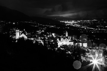 Aerial view of Assisi town (Umbria, Italy) and valley at night, with city lights and Santa Chiara church