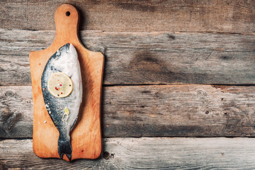 Seafood concept. Raw dorado fish with ingredients, lemon, spices over wooden cutting board over wood background. Top view. Healthy food diet. Food pattern.