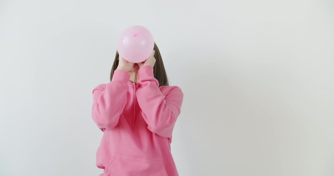 Young woman blowing a pink balloon