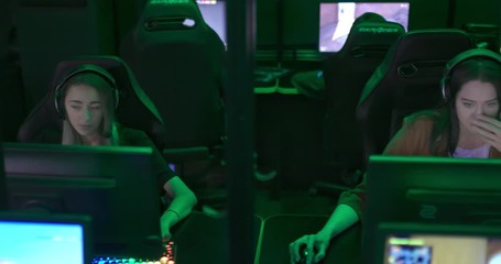 Beautiful girls play with guys in a computer club, online games. Team players are sitting in a row at computers in headphones. Modern cyber club. Camera span.