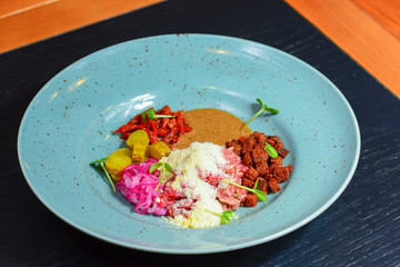 Vegetable salad with sause served on a blue plate on dark rustic wooden table in restaurant.