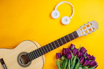 White guitar and white wireless headphones on the orange background, spring flowers, bunch of...