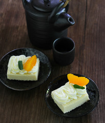 Small cake with butter cream and fresh mandarin orange served in black plate on old wood table background