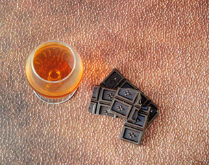 Glass goblet with cognac and broken chocolate bar on a brown abstract background.