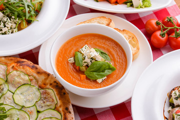 Pumpkin soup with feta cheese and vegetables served in white bowl topped with spinach with other Italian dishes