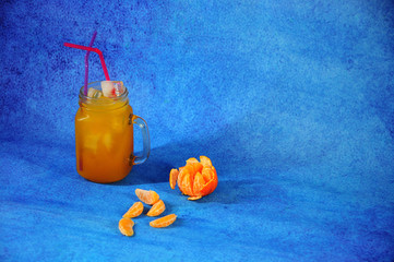 Glass mug of citrus juice with ice with slices of mandarin on a blue background. © Алексей Желтухин
