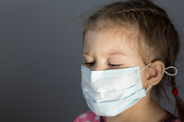 Portrait of caucasian child of three years old with mask on face looking down on gray background