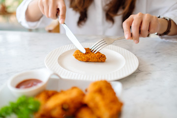 Closeup image of a woman using knife and fork to eat fried chicken in restaurant