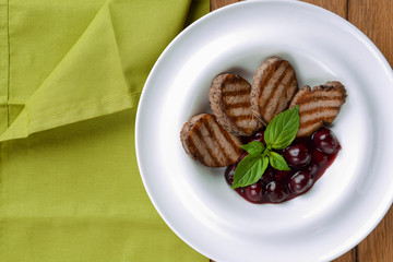 Grilled meat pieces with berry sauce served on a white plate over dark rustic wooden background. Italian cuisine.