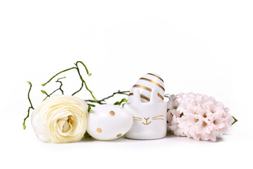 Easter eggs painted with metallic golden and white stripes and dots and cute easter egg cup in shape of bunny surrounded by spring flowers on white background