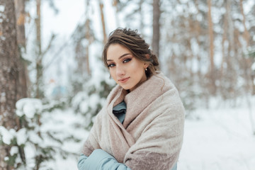 a beautiful girl in a wedding dress stands in a winter pine forest