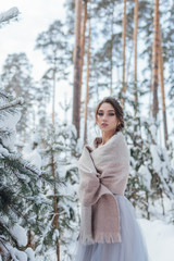 a beautiful girl in a wedding dress stands in a winter pine forest