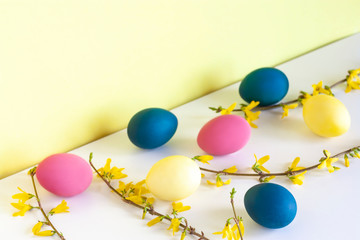 Modern easter composition with colored eggs and flowering branches on white desk near yellow wall. Easter concept. Copy space.