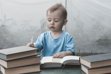 Portrait of a small child sitting at a table with books in the fresh air. Children and nature.