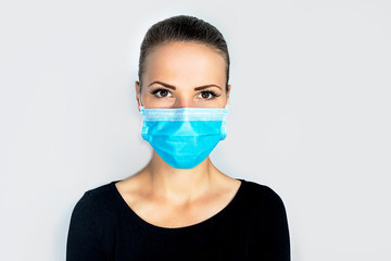 Young, beautiful woman in a medical mask, on a white background. A female in a sterile mask, looking directly at the camera. Epidemic and coronavirus, virus, pandemic