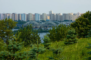 Obraz premium W oddali zielona trawa, drzewa, rzeka, most i miasto