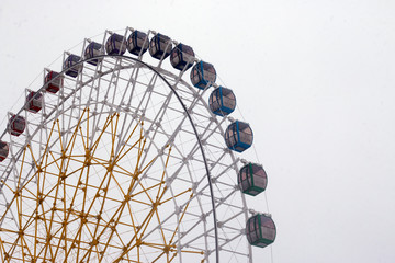 Ferris wheel in the fog. Multi-colored carousel cabins on a white sky background