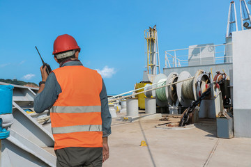crew worker on tanker ship, shipyard walkie- talkie or portable radio transceiver with mooring windlass for communication in hand holding control worker order for maintenance.