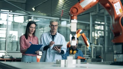 Science students are observing a robotic arm in action. Teamwork at an innovative technology laboratory. - Powered by Adobe