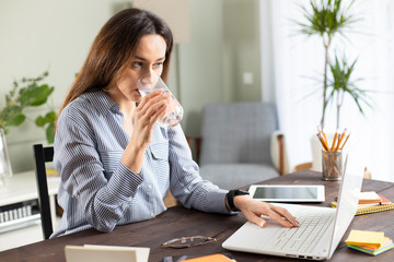 Freelancer young woman working at home and drinking water