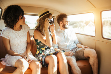 Three best friends travel in a minivan bus and explore new places. Two girls and one boy having good times. Taking pictures and selifies. Hugging and kissing eachother