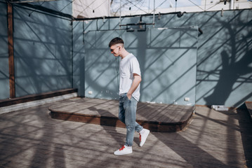 a young guy in dark glasses, a white t-shirt and blue jeans walks along the street and listens to music with headphones