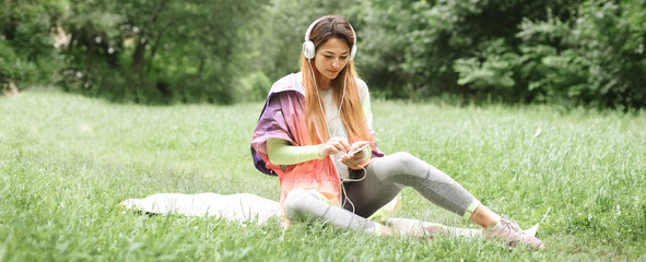 Beautiful sports girl resting in a park on a mat with headphones
