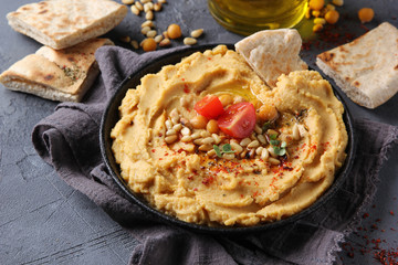 The concept of Oriental cuisine. Hummus with olive oil, spices, pine nut and tortillas. Chickpea appetizer in a black dish on a grey background. Turkish pea dish. Background image, copy space
