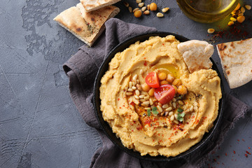 The concept of Oriental cuisine. Hummus with olive oil, spices, pine nut and tortillas. Chickpea appetizer in a black dish on a grey background. Turkish pea dish. Background image, copy space