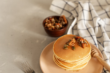 Stack of delicious pancakes with chocolate, honey, nuts and slices of banana on plate and napkin on wooden background