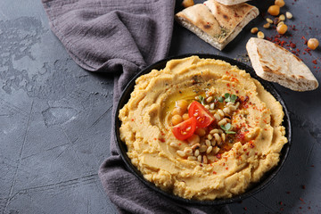 The concept of Oriental cuisine. Hummus with olive oil, spices, pine nut and tortillas. Chickpea appetizer in a black dish on a grey background. Turkish pea dish. Background image, copy space