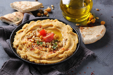 The concept of Oriental cuisine. Hummus with olive oil, spices, pine nut and tortillas. Chickpea appetizer in a black dish on a grey background. Turkish pea dish. Background image, copy space