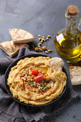 The concept of Oriental cuisine. Hummus with olive oil, spices, pine nut and tortillas. Chickpea appetizer in a black dish on a grey background. Turkish pea dish. Background image, copy space