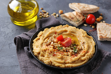 The concept of Oriental cuisine. Hummus with olive oil, spices, pine nut and tortillas. Chickpea appetizer in a black dish on a grey background. Turkish pea dish. Background image, copy space