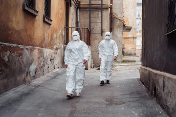 Obraz na płótnie Canvas People with protective suits and respirators walking outdoors along deserted, abandoned, ruined street. Coronavirus concept.