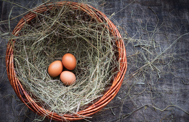 Three chicken eggs in a straw nest for Easter, rustic style, table, top view, copy space right