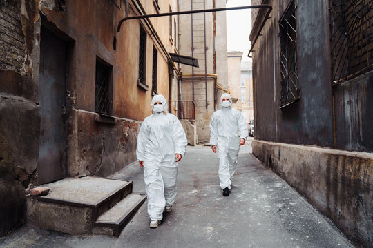 People with protective suits and respirators walking outdoors along deserted, abandoned, ruined street. Coronavirus concept.