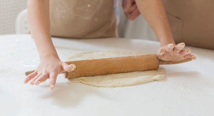 Granny's baking class. Unrecognizable child rolling dough with grandmother at table, closeup